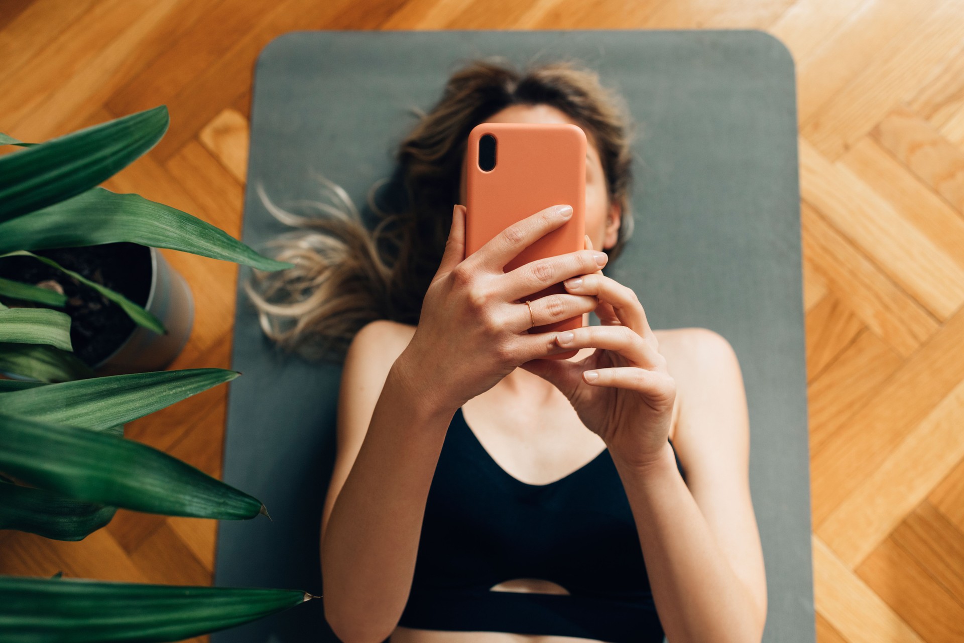 Young Woman Lying on a Yoga Mat and Using Her Smartphone